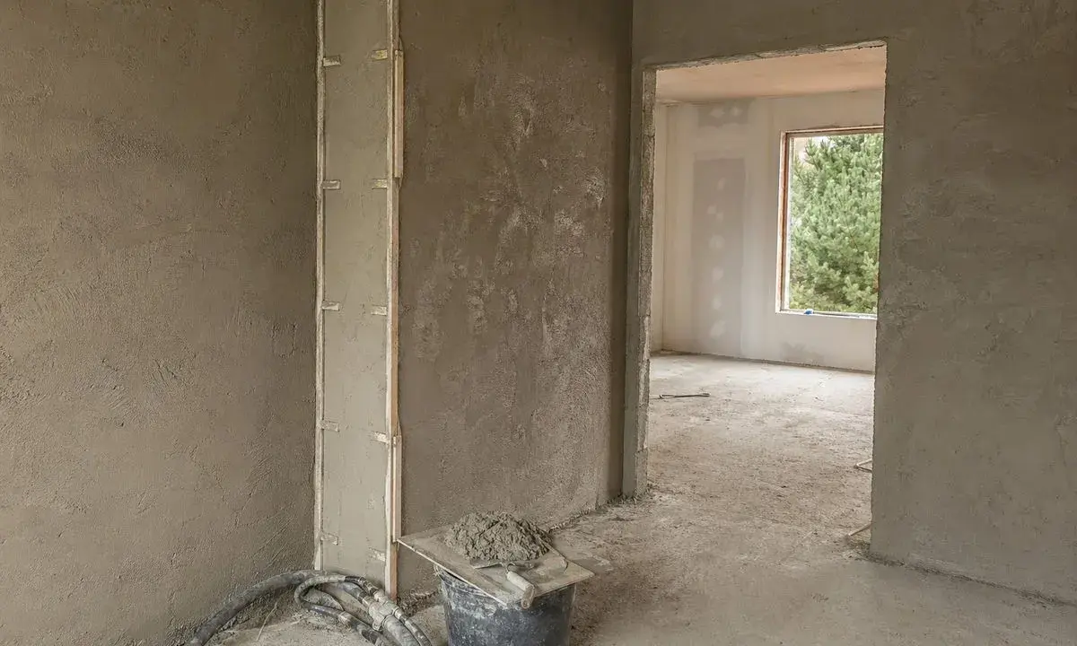 Ściany pokryte tynkami gipsowymi w nieogrzewanym domu. Widać wiadro z zaprawą i narzędzia.