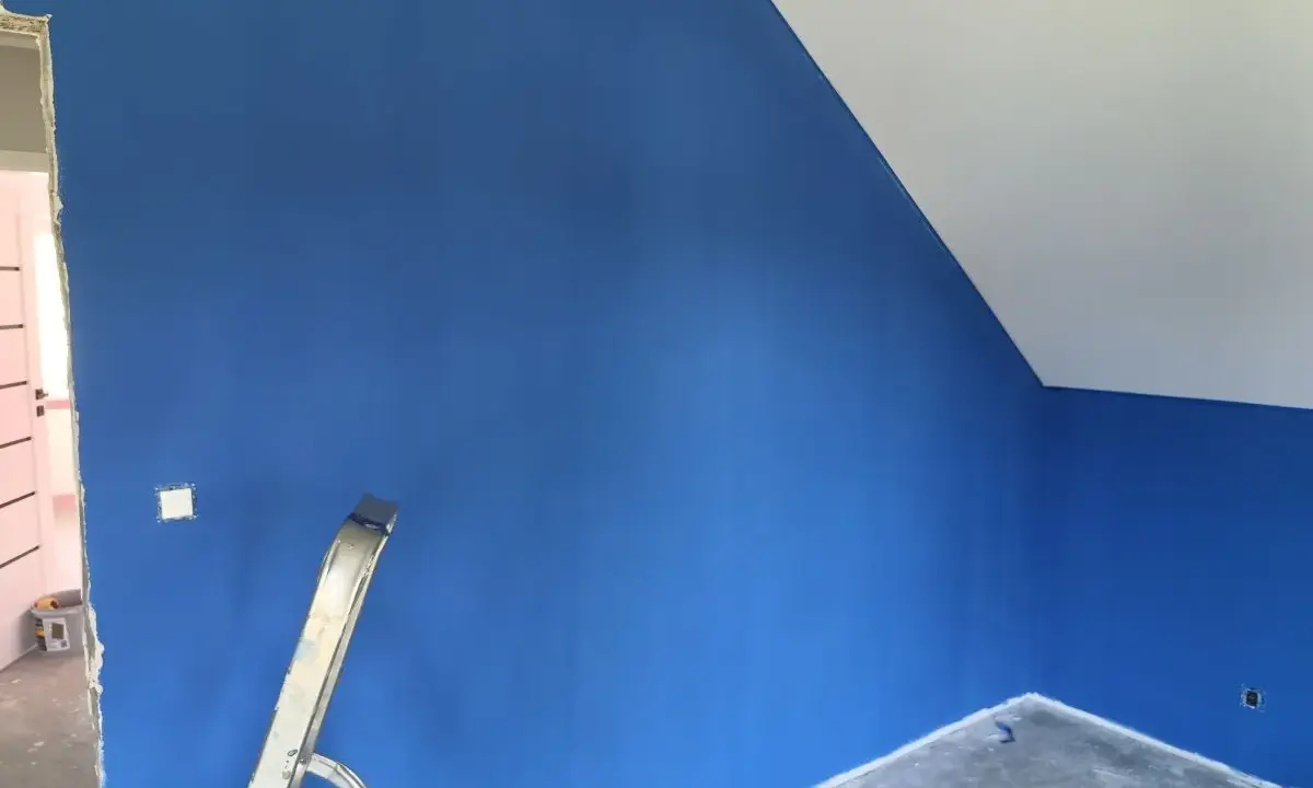 Niebieskie ściany z widocznymi smugami po malowaniu. Drabina stoi przy ścianie, a sufit jest biały.