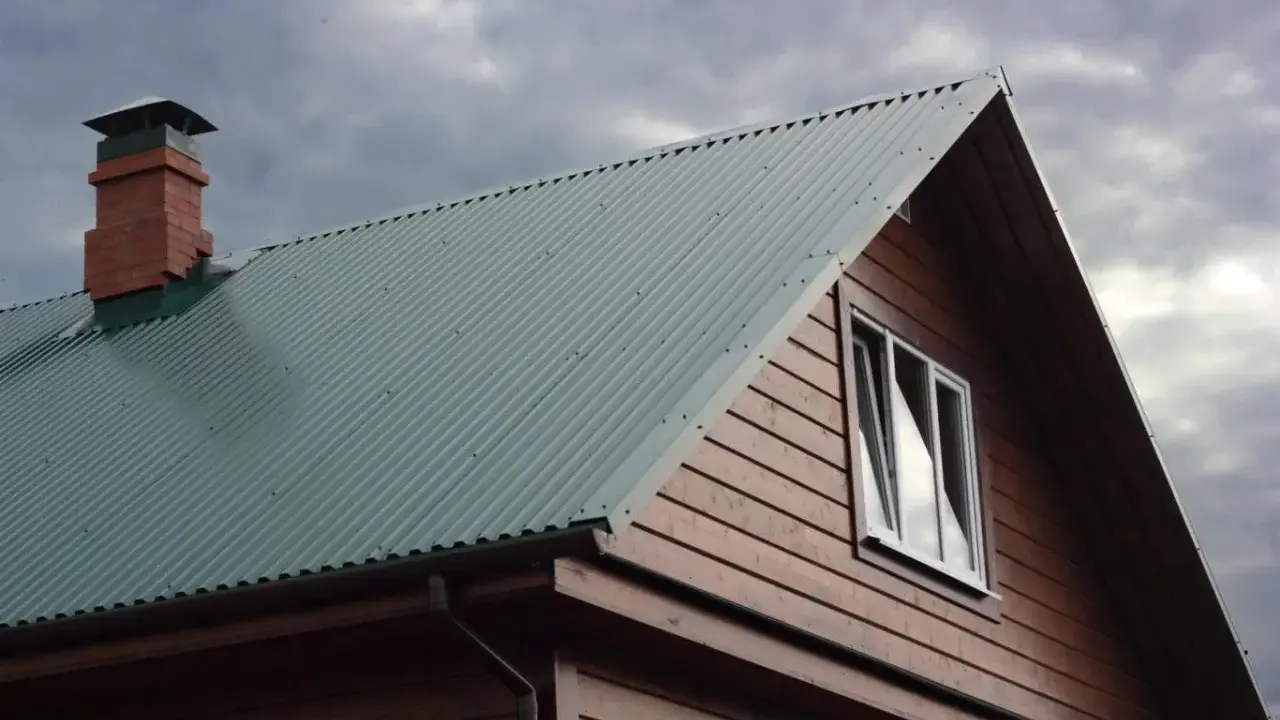 Dach domu pokryty zieloną blachą trapezową, z ceglanym kominem i drewnianą ścianą. Precyzyjne cięcie blachy trapezowej zapewnia estetykę.