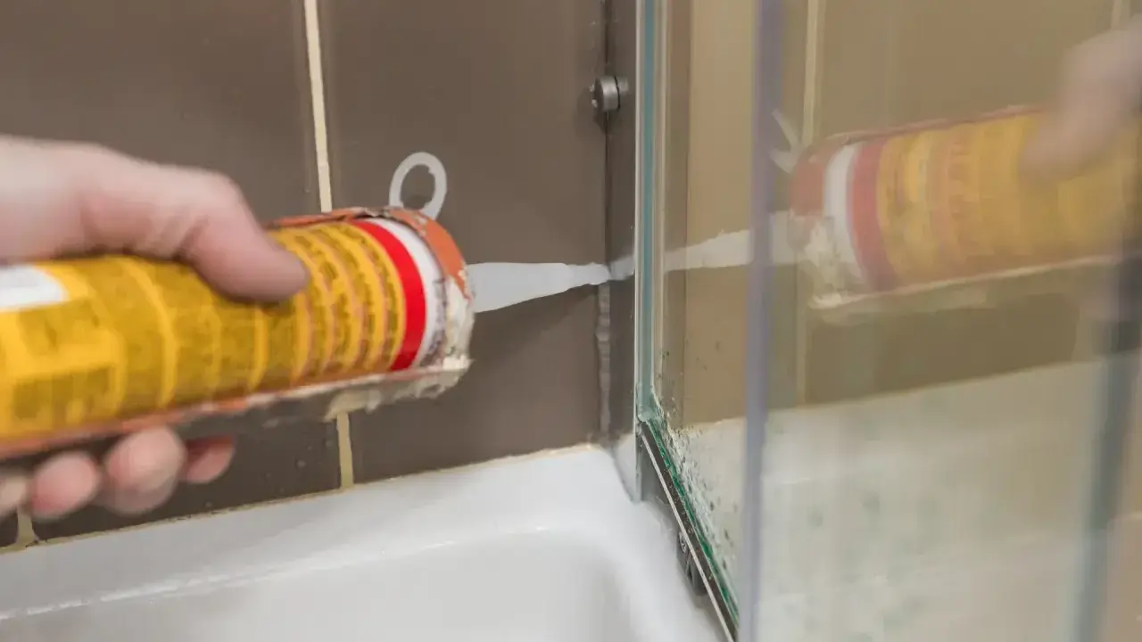 Uszczelnianie wanny silikonem. Ręka trzymająca pistolet z białą masą uszczelniającą, aplikując ją w narożniku prysznica.