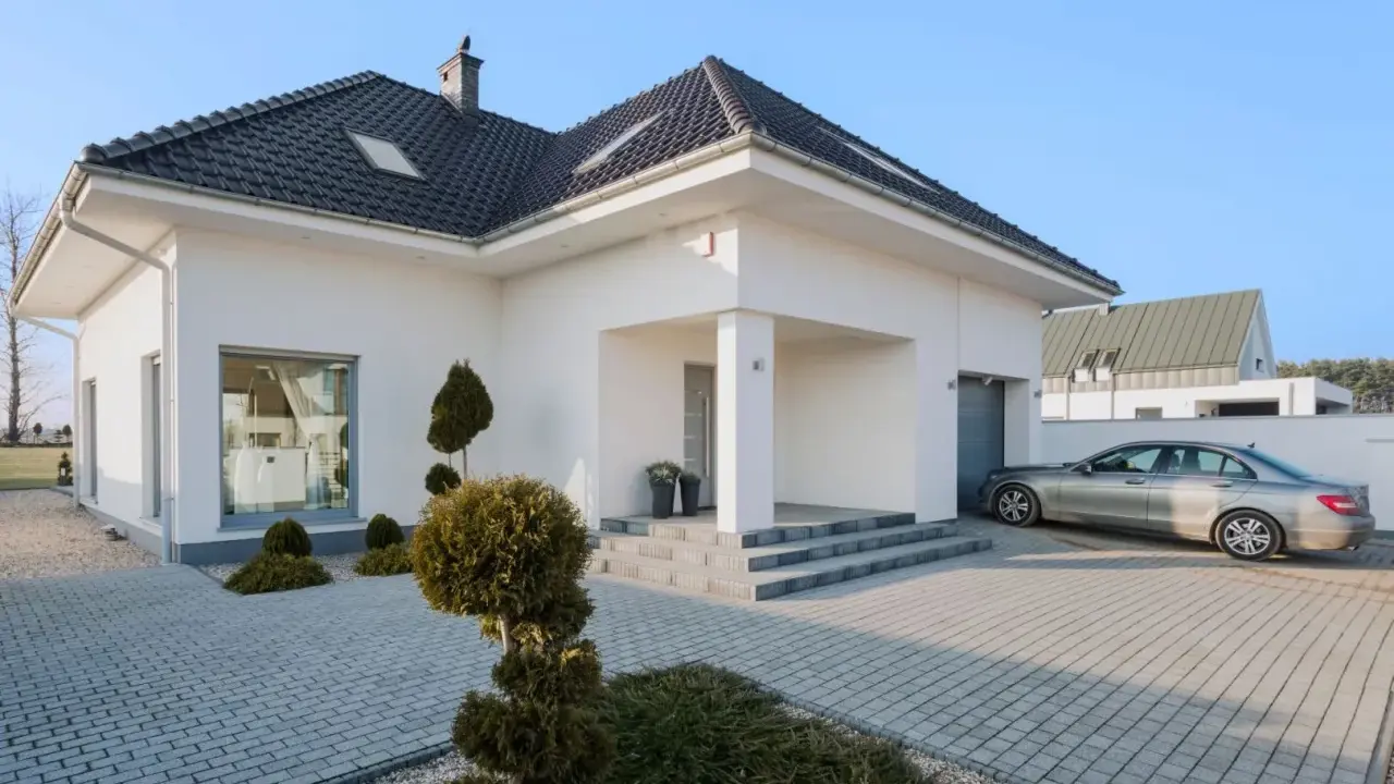 Nowoczesny dom z podjazdem wyłożonym starą kostką brukową, na którym stoi srebrny samochód.