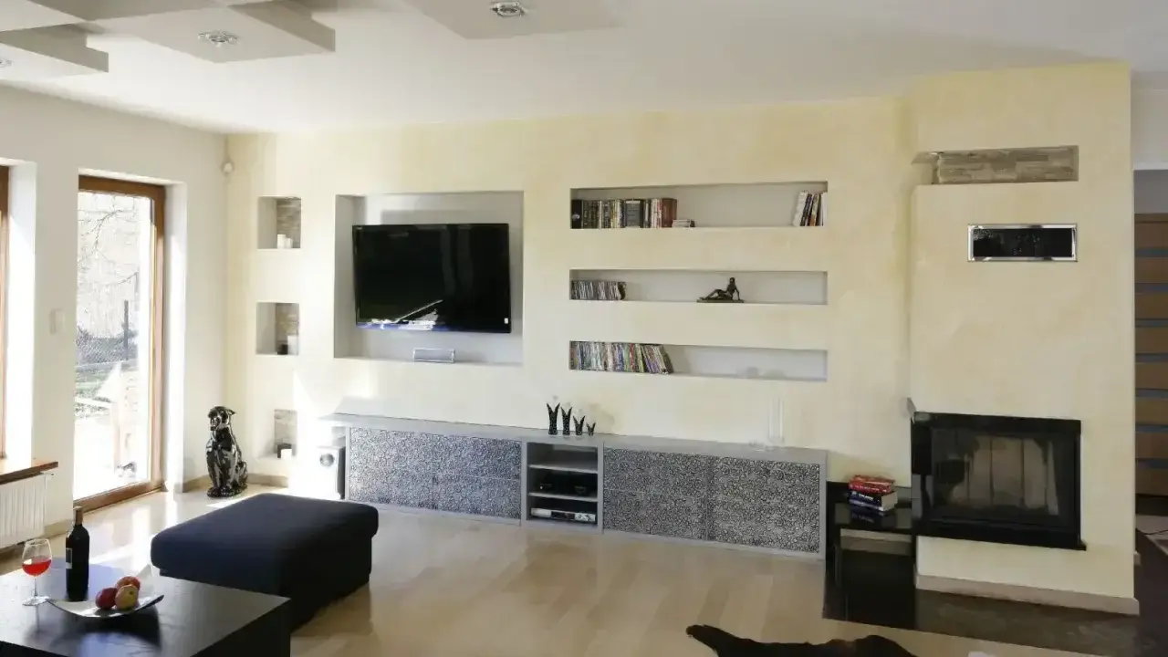 Nowoczesna zabudowa pod telewizor z regipsu z wnękami na książki i dekoracje.