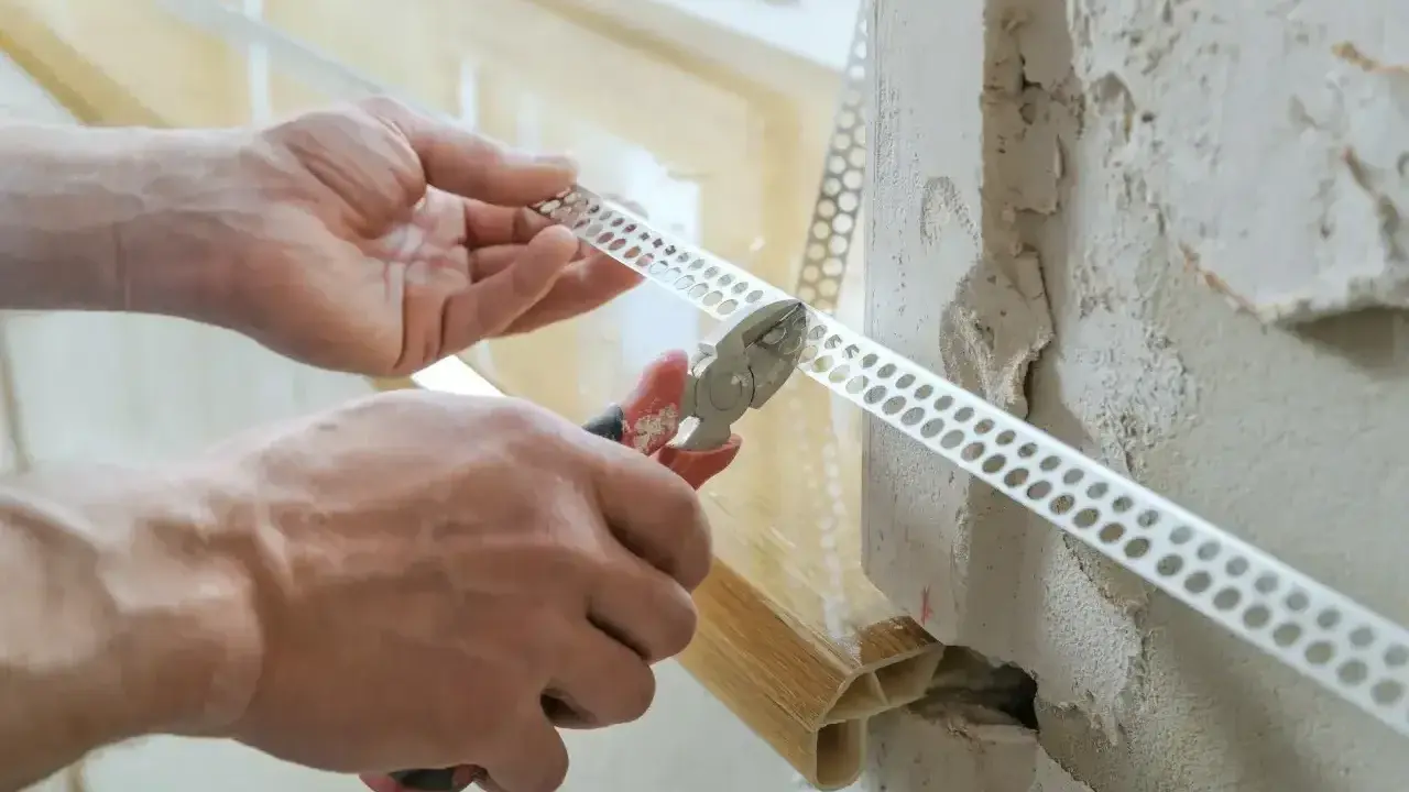 Ręce przycinają narożnikową listwę perforowaną, która posłuży jako wzmocnienie pod gips do narożników.