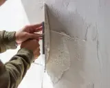 Ręce fachowca nakładają gładź na ścianę. Zastanawiasz się, ile za m2 gładzi zapłacisz?