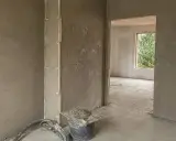 Ściany pokryte tynkami gipsowymi w nieogrzewanym domu. Widać wiadro z zaprawą i narzędzia.