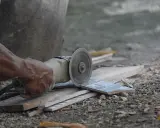 Ręka trzyma szlifierkę kątową, czym ciąć płytki gipsowe. W tle widać fragmenty płytek i gruzu.