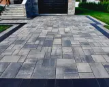 Elegancki chodnik z kostki granitowej w odcieniach szarości, z czarną obwódką, prowadzi do domu.