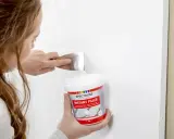 Kobieta używa szpachli i pojemnika z masą szpachlową Spectrum Instant Filler, by czym zaszpachlować dziurę w białej ścianie.