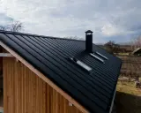 Czarny, metalowy dach z kominem i oknami dachowymi. Idealny przykład, jak dach symetryczny definicja może wyglądać w praktyce.