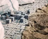 Kupa kostki brukowej czeka na ułożenie. Widać sporo piasku pod kostkę, gotowego do pracy.