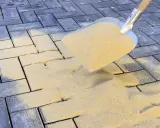 Łopata rozsypuje piasek na kostce brukowej. To kluczowy etap prac, który decyduje, jak długo ma leżeć piasek na kostce brukowej, by zapewnić stabilność.
