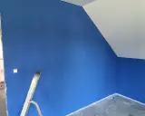 Niebieskie ściany z widocznymi smugami po malowaniu. Drabina stoi przy ścianie, a sufit jest biały.