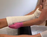 Nakładanie gipsowego opatrunku na nogę. Czy to gips do wody, czy wodą do gipsu? Dłoń w różowej rękawiczce modeluje materiał.