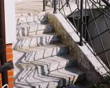 Kamienne stopnie schodów zewnętrznych, z widocznymi cieniami balustrady. Jaki beton na schody zewnętrzne? Ten wygląda na solidny.