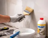 Gruntowanie ścian z płyt gipsowych przed nałożeniem gładzi. Pędzel nakłada biały preparat.