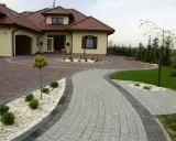 Eleganckie układanie kostki brukowej wokół nowoczesnego domu. Dwa rodzaje kostki tworzą efektowną ścieżkę i podjazd.