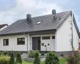 Nowoczesny dom z białymi ścianami i szarym dachem o nachyleniu 45 stopni. Na dachu komin i antena satelitarna.