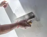 Ręka z kielnią wygładza gładką powierzchnię ściany, tworząc idealnie równą płaszczyznę.