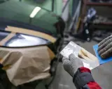 Ręce w rękawiczkach nakładają szpachlę elastyczną na pęknięcia karoserii samochodu.