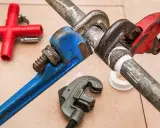 Narzędzia hydrauliczne i czerwony trójnik. Zastanawiasz się, czym zakleić dziury po hydrauliku? Taśma teflonowa i klucze nastawne pomogą.