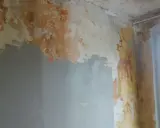 Ściana z odpadającą farbą i tynkiem, przygotowywana do remontu. Widać fragmenty szarej gładzi, które pomogą jak naprawić kratery w gładzi gipsowej.