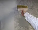 Ręka w białej bluzie nakłada preparat pędzlem na popękaną gładź, by ją naprawić.