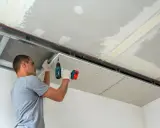 Montaż sufitu z karton gipsu. Pracownik przykręca płyty do stelaża, tworząc gładką powierzchnię.