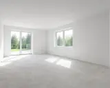 Puste, jasne pomieszczenie z betonową podłogą i białymi ścianami. Okna wychodzą na zielony ogród. Czekam, po jakim czasie druga warstwa gładzi będzie gotowa.