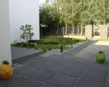 Nowoczesny ogród z kamieniami zamiast trawnika, z geometrycznymi donicami i ścieżką z płyt.