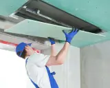 Pracownik montuje płytę gipsowo-kartonową, dbając o minimalną grubość ścianki.