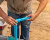 Ręce montują niebieskie rury PVC, przygotowując je do klejenia.