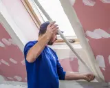 Budowlaniec montuje narożniki aluminiowe na skosach poddasza, przygotowując je do tynkowania.