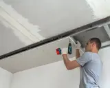 Mężczyzna przykręca płytę kartonowo-gipsową do stelaża sufitowego. Do cięcia karton gips używa się specjalnych narzędzi.