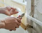 Ręce przycinają narożnikową listwę perforowaną, która posłuży jako wzmocnienie pod gips do narożników.