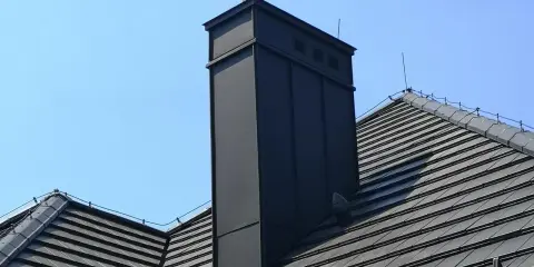 Nowoczesna obróbka blacharska komina na dachu z dachówki. Schemat montażu zapewnia estetykę i trwałość.