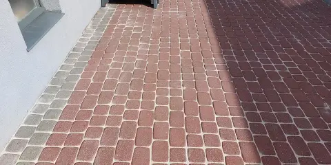 Ubijanie kostki z piaskiem czy bez? Świeżo ułożona ścieżka z czerwonej i szarej kostki brukowej przy domu, z drewnianymi schodkami.