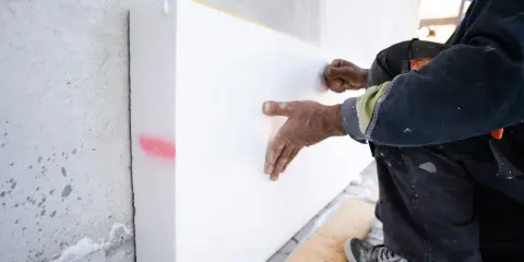 Ręce pracownika przytwierdzają styropian do ściany. To dobry sposób, czym wypełnić bruzdy z kablami, zapewniając izolację.