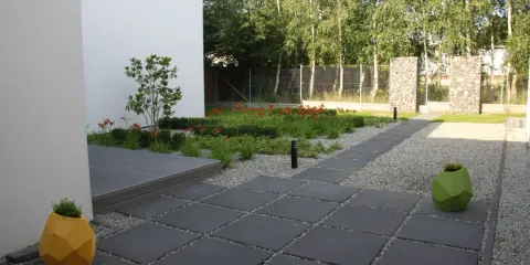 Nowoczesny ogród z kamieniami zamiast trawnika, z geometrycznymi donicami i ścieżką z płyt.