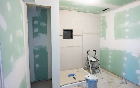 W pomieszczeniu w trakcie remontu, przygotowywanym do łazienki, widać płyty gipsowe na ścianach i suficie. W narożniku stoi drabina, a na podłodze wiadro i wałek malarski. To etap, gdy zastanawiamy się, jak zabezpieczyć płyty gipsowe przed wilgocią.