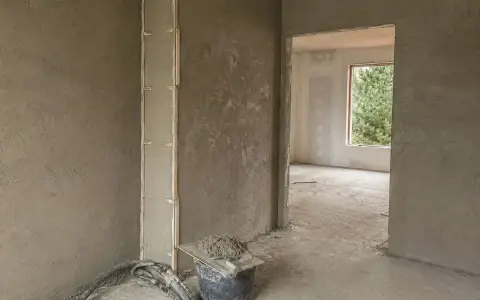 Ściany pokryte tynkami gipsowymi w nieogrzewanym domu. Widać wiadro z zaprawą i narzędzia.