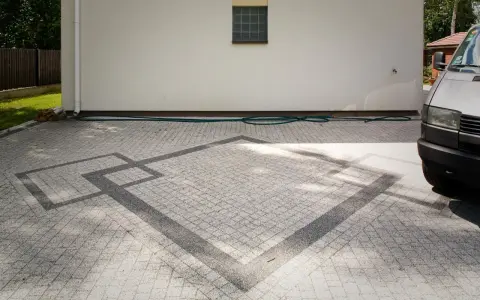 Nowoczesne układanie kostki na grysie z geometrycznym wzorem. Wjazd do domu z szarej kostki.