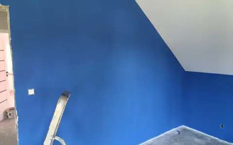 Niebieskie ściany z widocznymi smugami po malowaniu. Drabina stoi przy ścianie, a sufit jest biały.