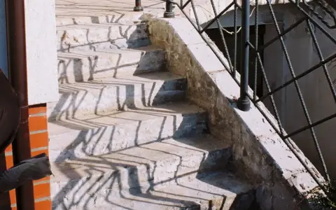 Kamienne stopnie schodów zewnętrznych, z widocznymi cieniami balustrady. Jaki beton na schody zewnętrzne? Ten wygląda na solidny.