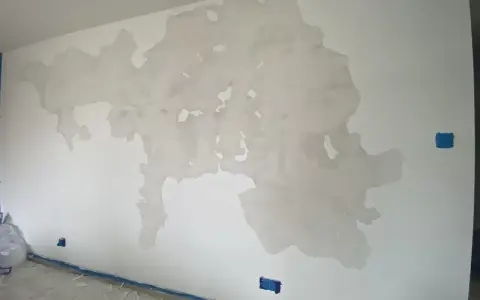 Duże płaty odparzonej farby na białej ścianie, przypominające mapę. Na podłodze resztki farby i niebieska taśma.