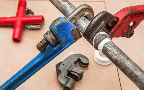 Narzędzia hydrauliczne i czerwony trójnik. Zastanawiasz się, czym zakleić dziury po hydrauliku? Taśma teflonowa i klucze nastawne pomogą.