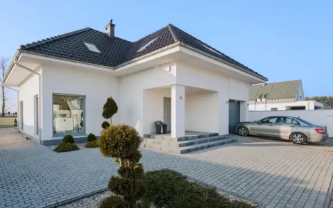 Nowoczesny dom z podjazdem wyłożonym starą kostką brukową, na którym stoi srebrny samochód.