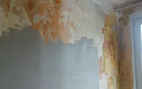 Ściana z odpadającą farbą i tynkiem, przygotowywana do remontu. Widać fragmenty szarej gładzi, które pomogą jak naprawić kratery w gładzi gipsowej.