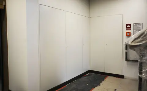 Nowoczesna zabudowa szachtu w bloku, z białymi drzwiami i dyskretnymi uchwytami. Na ścianie widoczny alarm przeciwpożarowy.