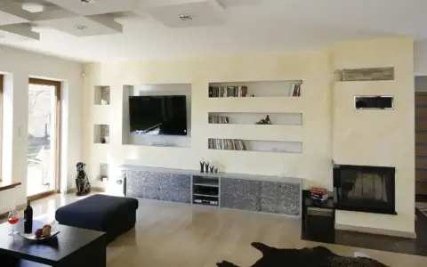 Nowoczesna zabudowa pod telewizor z regipsu z wnękami na książki i dekoracje.