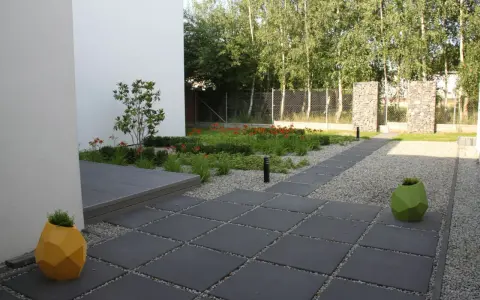 Nowoczesny ogród z kamieniami zamiast trawnika, z geometrycznymi donicami i ścieżką z płyt.